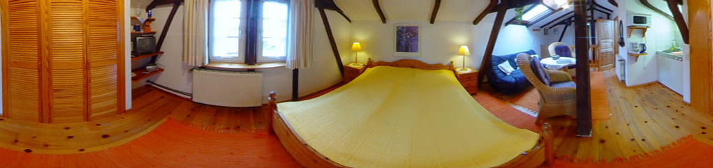 Foto der Ferienwohnung 5 im Obergeschoss mit Sitzecke im Hintergrund und Doppelbett im Vordergrund, und Pantryküche